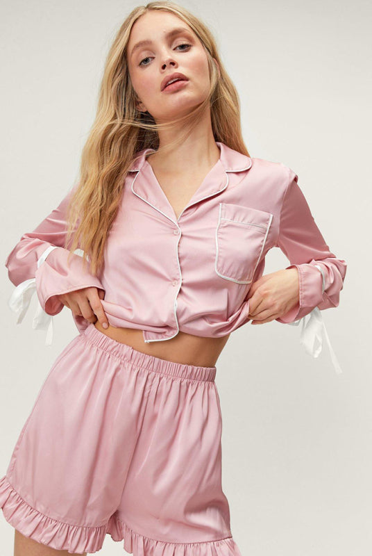 A woman wearing a pink long-sleeved pajama top with a lapel collar and matching shorts, both with ruffle details.